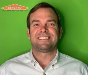 Man in polo shirt in front of green background with orange logo in top left.